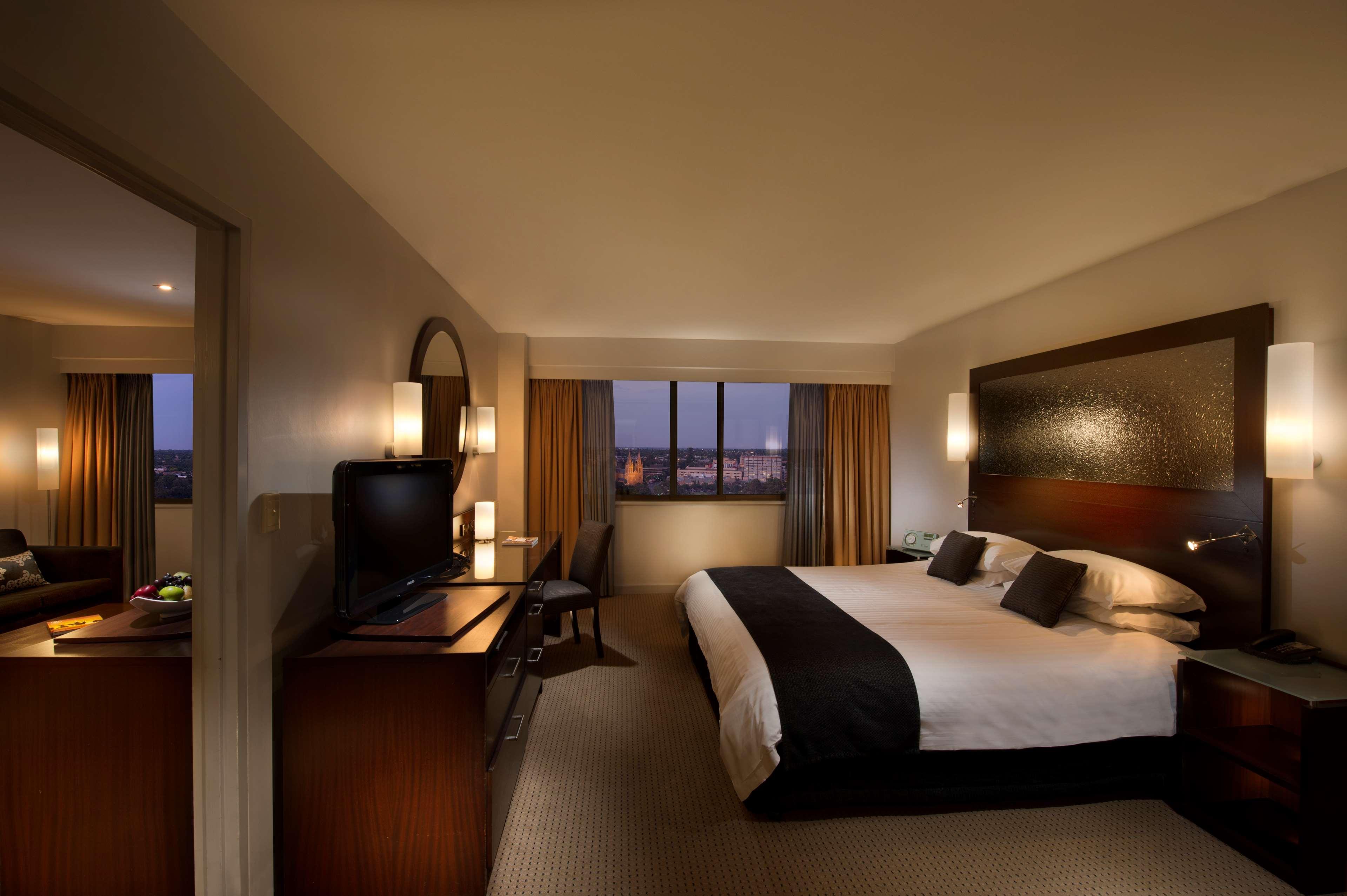 Stamford Plaza Adelaide Hotell Eksteriør bilde The photo features a modern hotel room that includes a large bed with dark and light bedding, complemented by two pillows. The room is well-lit with warm lighting and has a contemporary aesthetic. To one side, there is a wooden dresser with a flat-sc