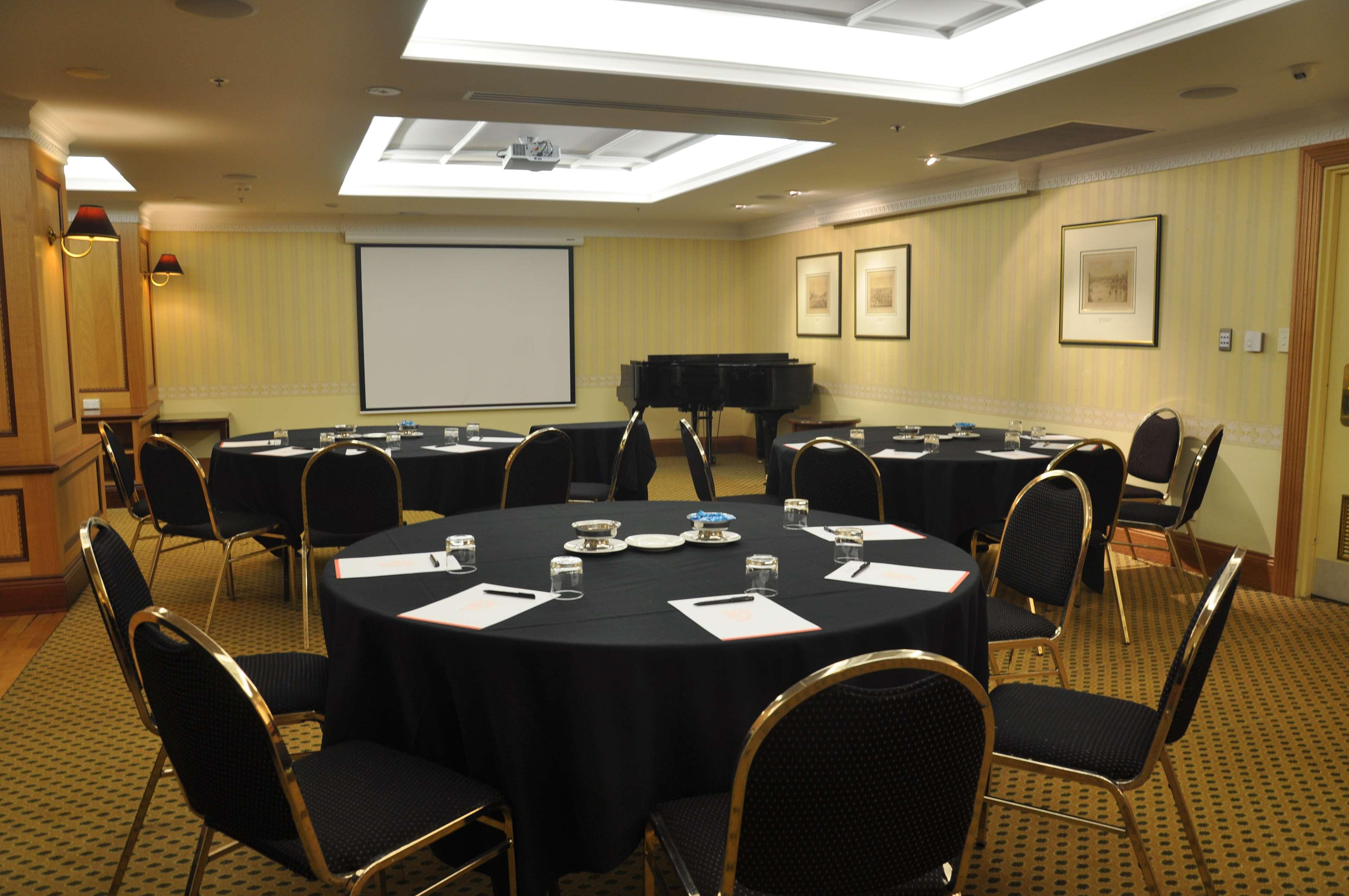 Stamford Plaza Adelaide Hotell Eksteriør bilde The photo shows a conference room set up for a meeting or presentation. There are several round tables covered with black tablecloths, each surrounded by black upholstered chairs. On the tables, there are notepads and glasses of water, indicating tha