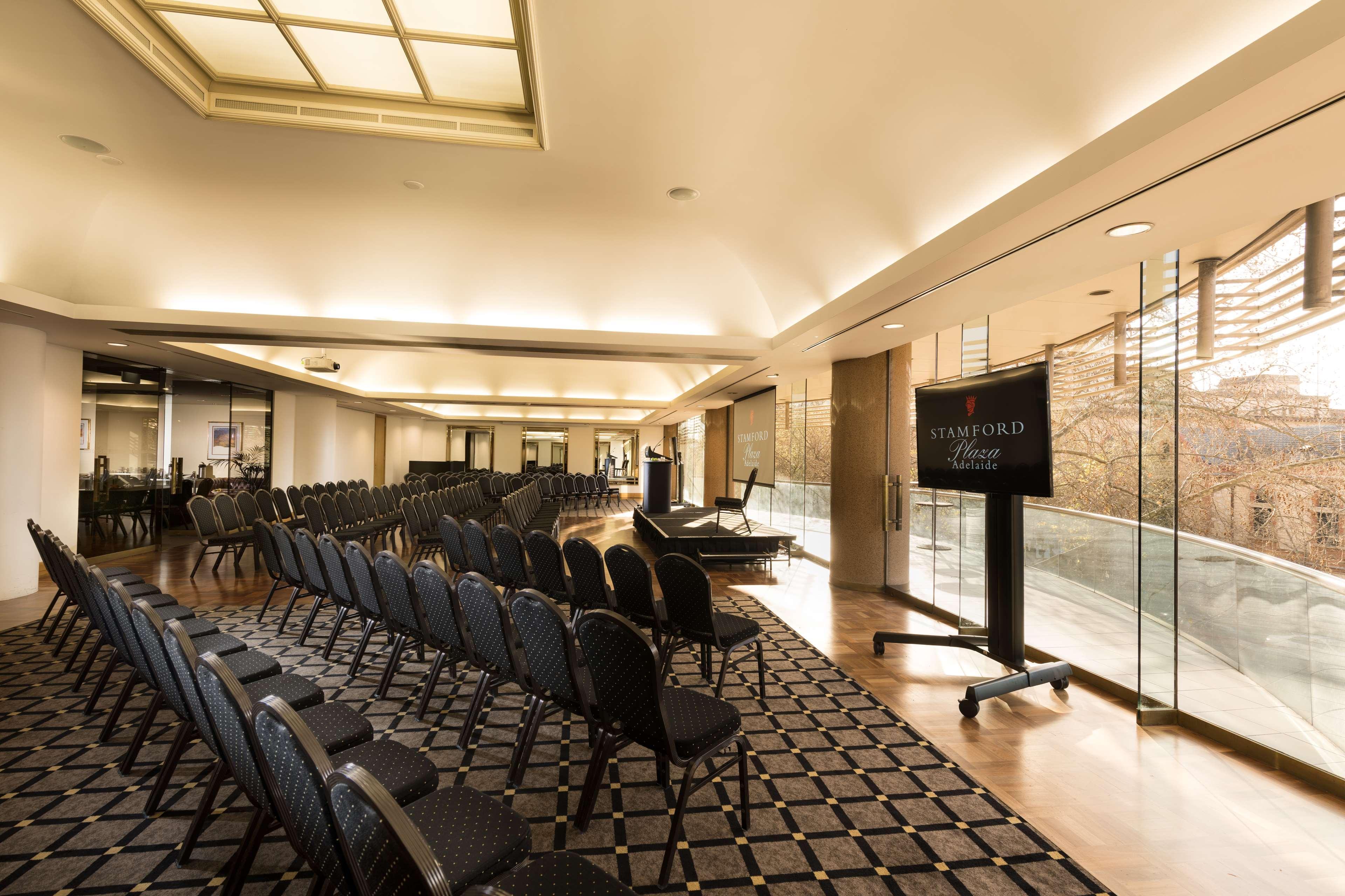 Stamford Plaza Adelaide Hotell Eksteriør bilde The photo shows a large, elegantly designed event space or meeting room. There are rows of black chairs set up facing a presentation area. The flooring features a patterned carpet, and large windows allow natural light to enter the room. On one side,