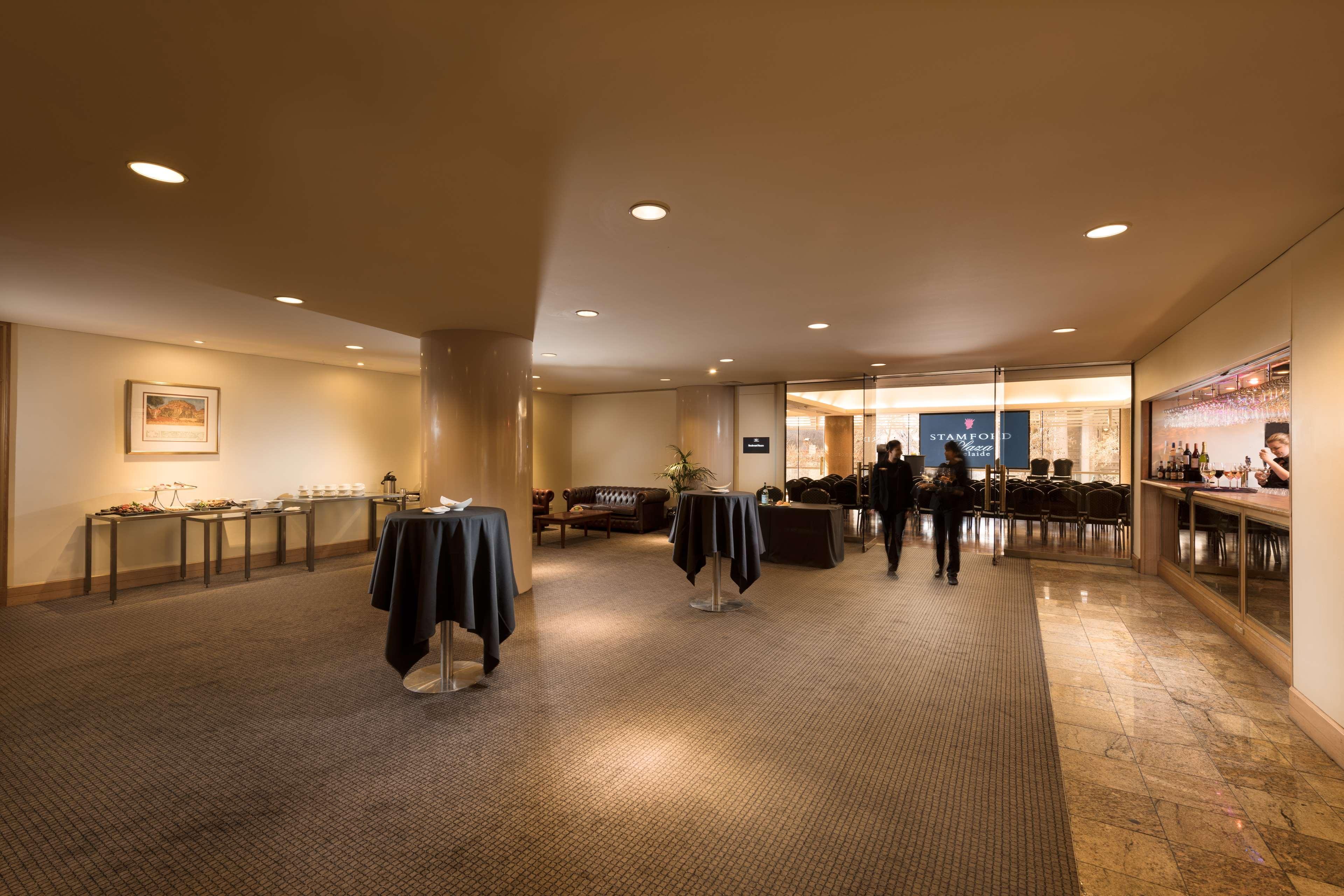 Stamford Plaza Adelaide Hotell Eksteriør bilde The image shows an indoor space that appears to be a lounge or reception area. There are several round tables with dark tablecloths positioned throughout the room. The floor is carpeted, and the lighting is warm and somewhat dim. In the background, t