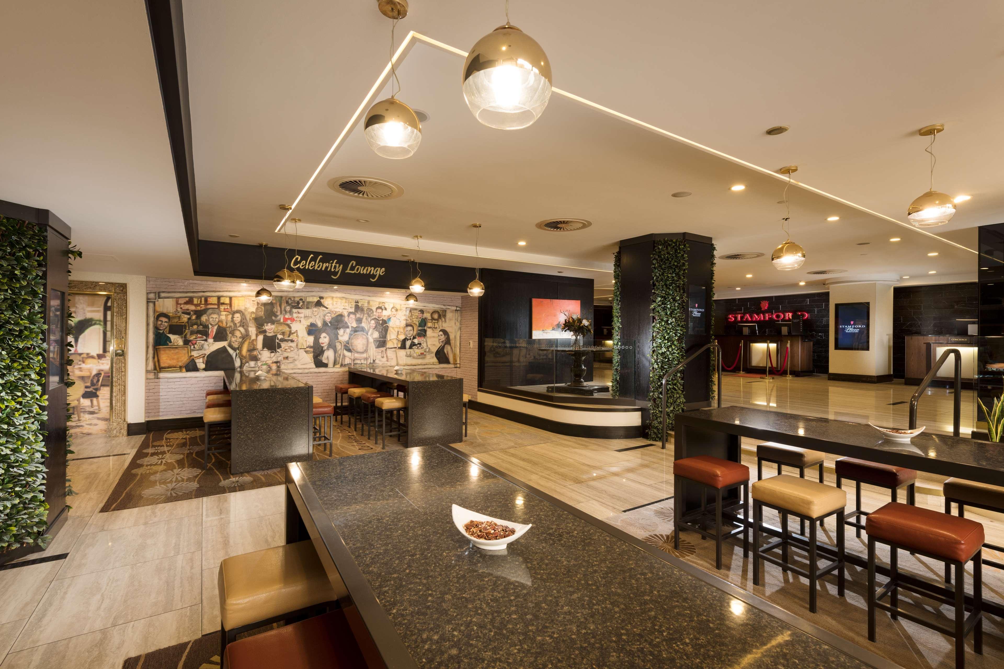 Stamford Plaza Adelaide Hotell Eksteriør bilde The photo shows a modern and stylish interior of a lounge or restaurant area. Prominent features include a long dark countertop with bar stools, and several pendant lights hanging from the ceiling. In the background, there is a mural or artwork that 